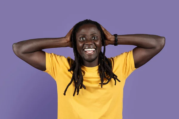 驚きの長い髪の若いアフリカ系アメリカ人の男で黄色のTシャツを頭に触れ 紫色のスタジオの背景にカメラで笑顔 人間の感情の概念 — ストック写真