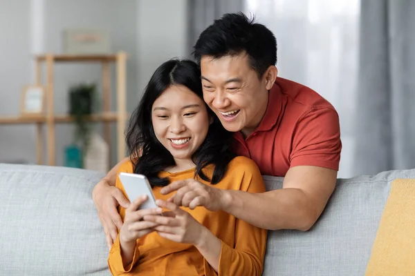 Χαμογελώντας Κινέζοι Σύζυγοι Χρησιμοποιώντας Κινητό Τηλέφωνο Στο Σπίτι Ψωνίζοντας Online — Φωτογραφία Αρχείου