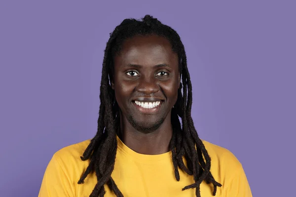 幸せなハンサムなアフリカ系アメリカ人の百万人の男の閉鎖写真紫のスタジオの背景に笑みを浮かべて長い編組 黄色のTシャツを着ている 黒人のライフスタイルコンセプト — ストック写真