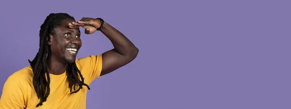 黄色のTシャツを保持ヤシの目の横にある コピースペースを見て 紫色のスタジオの背景に隔離された 素敵な広告をチェックする興奮した長髪の千年黒人男性 クローズアップ パノラマ — ストック写真