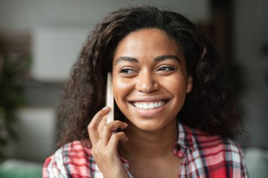 Telefonla arayan, minimalist oturma odasındaki arkadaşıyla konuşan neşeli siyahi genç kadının portresi, kapat. Cihazda uzaktan iletişim, dedikodu ve iyi haber, yaşam tarzı, yeni normal