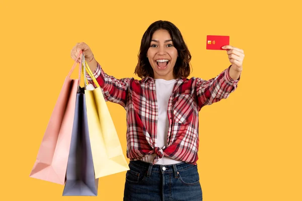 穿着休闲装 头戴彩色购物袋 头戴红色塑料信用卡 背景为黄色的中东美女 兴奋极了 无限购物 销售概念 — 图库照片