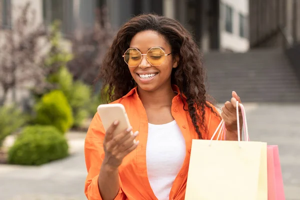 パッケージやスマートフォンで幸せな若い黒人女性の顧客の肖像画は オンラインショッピング 素晴らしい広告 提供し 街の通りでキャッシュバックをお楽しみください 巨大な販売とファッションブログ 新しい通常とリモートで注文 — ストック写真