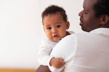 Gülümseyen Afrikalı genç bir Amerikalı baba kucağında tatlı bir bebek, siyah babayla ilgilenen sevimli küçük oğluna ya da kızına sarılıp evde kaynaşırken, yakın plan portresi, kopyalama uzayı