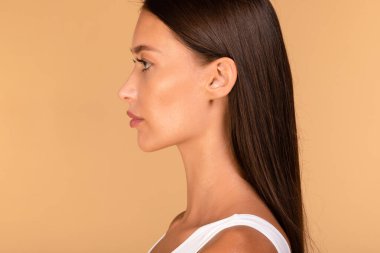 Bej renkli stüdyo arka planında poz veren, boş alana bakan beyaz bir kadının yan görüntüsü. Reklam afişi için kadın portresi