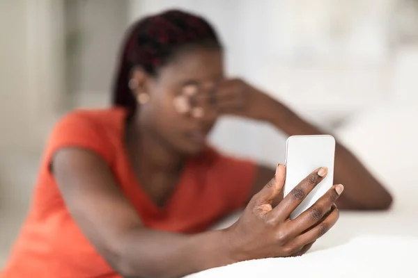 Upset Black Lady With Smartphone In Hand Sitting At Home, Depressed Young African American Female Holding Modern Cellphone And Covering Eyes, Got Bad News Or Unplesant Message, Closeup Shot