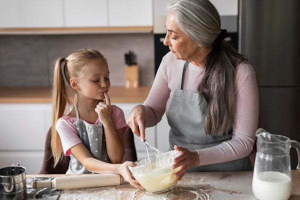 快乐的高加索小孙女和成熟的祖母沾满面粉 品尝烘烤面团 一起在现代厨房的内部享乐 糖果饼干在家做饭和上课 — 图库照片
