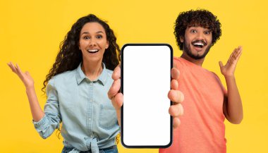Harika bir teklif. Şaşırmış Arap çift kamerada beyaz ekranlı büyük boş akıllı telefonu gösteriyor Orta Doğulu genç adam ve kadın, Mobil Mobil Uygulamaya Duygusal Tepki gösteriyor.