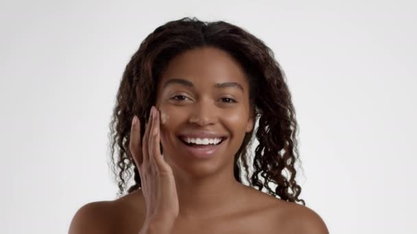 季节性面部护理 非洲裔美国妇女在面颊 白色画室背景 慢动作上应用护肤滋养乳膏的近照 — 图库视频影像