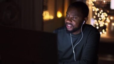 Kendi kendine eğitim kavramı. Genç, pozitif, Afro-Amerikalı bir adam kulaklıkla webinar izleyip not alıyor, gece geç saatlerde evde çalışıyor, çekim takip ediyor, yavaş çekim yapıyor, boş alan arıyor.