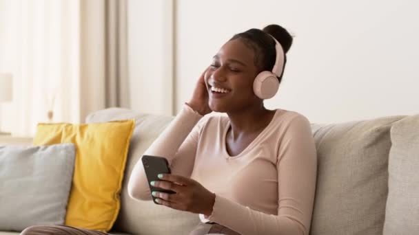 在线流媒体服务 年轻快乐的非洲裔美国女人 在耳机里听音乐 在智能手机上上网 选择最喜欢的音乐 跟踪镜头 慢动作 自由自在的空间 — 图库视频影像