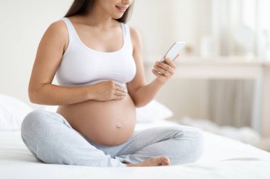 Bir bayanın yatakta oturmasını, akıllı telefon kullanmasını, alet ekranına bakmasını, gülümsemesini, internetten alışveriş yapmasını hamile kadınlar için mobil uygulama kullanmasını, yatak odasının içini, fotokopi alanı olan panorama kullanmasını beklemek.