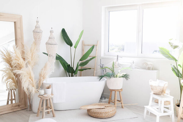 Stylish Interior Of Light Bathing Room With Rustic Decorations In Boho Style, Cozy Spacious Bathroom With Natural Green Plants Near Window And Big White Bath Tube Inside, Free Space