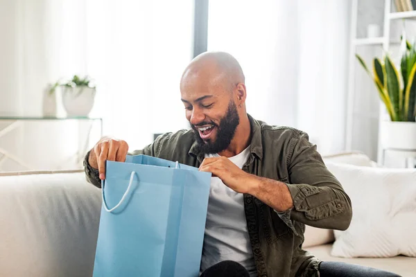 ショッピングコンセプト 衣料品店から配達されたカラフルな買い物袋を見て幸せなラテン人は 自宅でソファに座っています 成熟した男性のお客様から注文を受ける店 — ストック写真