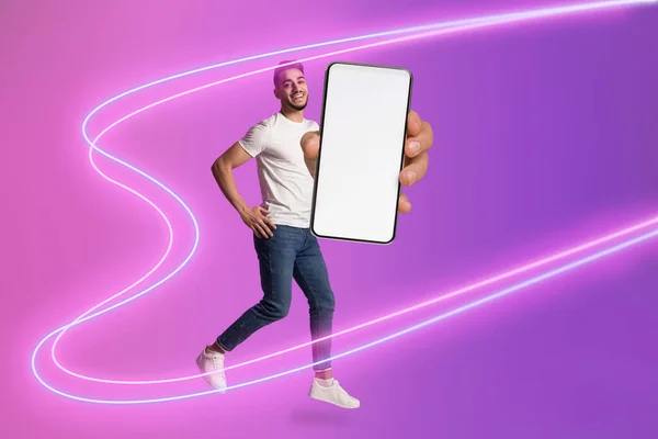 広告のための白い空白の画面を持つブランドの新しいスマートフォンを示すカジュアルな服装で積極的なハンサムな若い中東の男 ネオンライトでポーズ コラージュ モックアップ フル長さの写真 — ストック写真