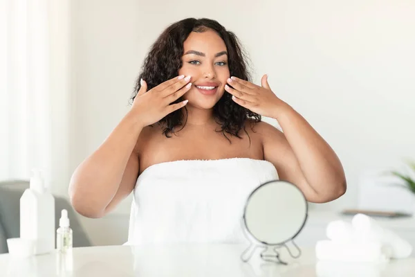 若いアフリカ系アメリカ人プラスサイズの女性は彼女の顔に触れながら 寝室で顔の治療を行います 彼女の肌の状態を楽しんで カメラで笑顔 コピースペース — ストック写真