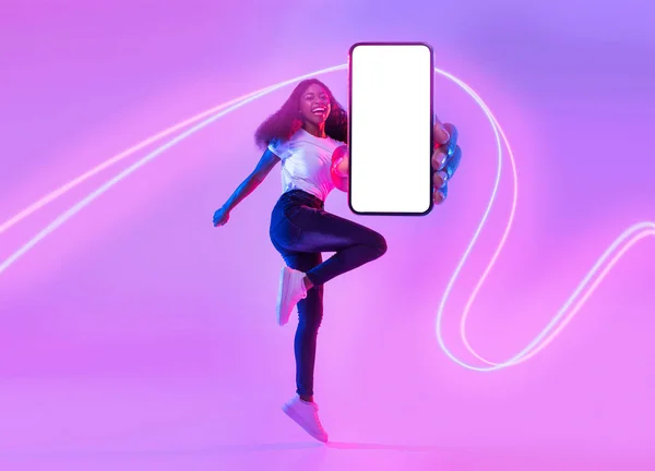 穿着休闲装的年轻漂亮的非洲裔美国女人 带着霓虹灯在空中跳着手机 在白色的屏幕上展示广告 复制的空间 — 图库照片