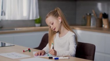 Modern çocuklar boş vakit geçirir. Tasasız küçük kız mutfakta resim çiziyor ve kablosuz kulaklıklarla müzik dinliyor, yavaş çekim, boş alan