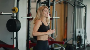 Kardiyo testi. Aktif orta yaşlı bir kadın koşuyor ve spor bileziğine bakıyor. Faaliyetlerini ve kalp atışlarını kontrol ediyor. Spor salonunda egzersiz yapıyor.