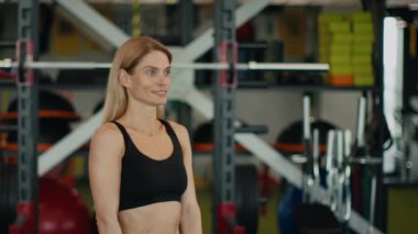 Pazı egzersizi. Pozitif orta yaşlı kadın portresi. Dambılları kaldırıyor, spor salonunda egzersiz yapıyor, gülümsüyor, yavaş çekim, boş alan.