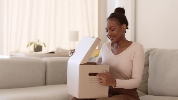 Rozpakowywanie Młoda Szczęśliwa Afrykańska Kobieta Otwierająca Pudełko Dostawą Patrząca Niebieską — Wideo stockowe