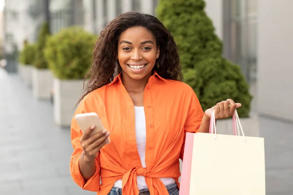デジタル広告とオファー スマートフォンやパッケージで若い黒人女性を笑顔 市内でリモートでオンラインショッピングをお楽しみください ガジェットで購入を注文する 社会的距離 販売と現代的なアプリの金融 — ストック写真