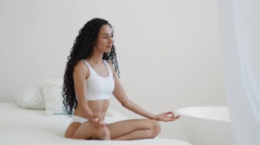 Sabah meditasyonu. Genç barışçıl kadın evde meditasyon yapıyor, lotus pozisyonunda oturuyor gözleri kapalı ve nefes alıyor, yavaş çekim, boş alan