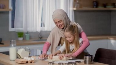 Ev yapımı aşçılık. Mutlu Müslüman anne küçük kızıyla turta pişiriyor, hamuru birlikte yuvarlıyor, ağır çekimde, boş alanda.