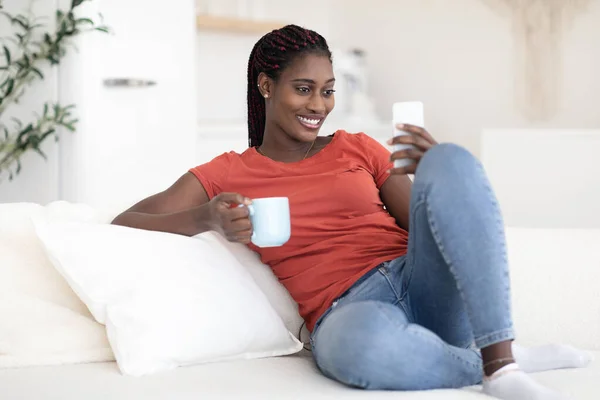 Inländische Erholung Lächelnde Schwarze Auf Couch Mit Smartphone Und Kaffee — Stockfoto
