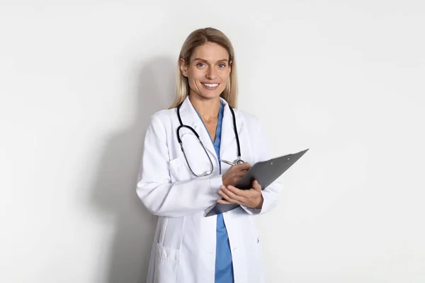 医疗服务 穿着制服 手持剪贴板 看着相机的美丽微笑的女医生的画像 她是一位站在白底 复制空间的专业女医生 — 图库照片