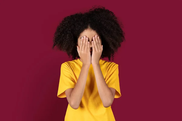 Przerażona Afrykańska Nastolatka Krzaczastymi Włosami Przykrywająca Twarz Dłońmi Odizolowana Bordowym — Zdjęcie stockowe