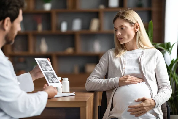 男医生在办公室会面时向忧心忡忡的孕妇展示婴儿超声图像 专业生殖内科医生向女性病人解释检查结果 — 图库照片