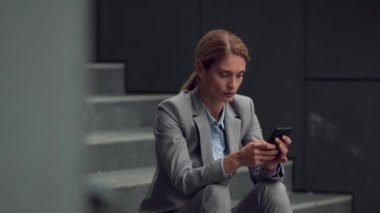 İş günlerinde kişisel sorunlar. Dizüstü bilgisayarda yazı yazan endişeli kadın, aile sorunlarını tartışıyor, ofis binasının yanındaki merdivenlerde oturuyor, çekim takibi yapıyor, yavaş çekim yapıyor.