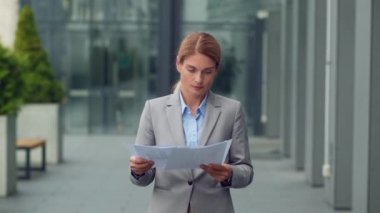 Meşgul orta yaşlı iş kadını proje belgelerini inceliyor, ofis binasının yanında kağıtlarla yürüyor, çekim takip ediyor, yavaş çekim, serbest alan