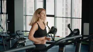 Kardiyo çalışması. Modern spor salonunda koşu bandında koşan aktif orta yaşlı kadın sporcunun kapalı portresi, yavaş çekim, boş alan