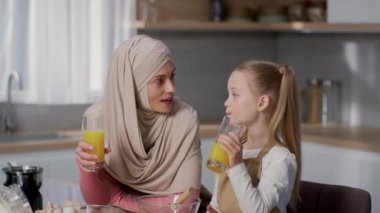 Sağlıklı ev alışkanlıkları. Mutlu Müslüman anne ve küçük kızının portresi. Mutfakta portakal suyu içip gülüyorlar, ağır çekimde.
