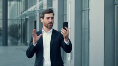 Modern ticaretin hareketliliği. Takım elbiseli profesyonel iş adamının iş arkadaşlarıyla sohbet ederken, ofis binasının yakınında yürürken, projeyi tartışırken, yavaş çekim, serbest alan