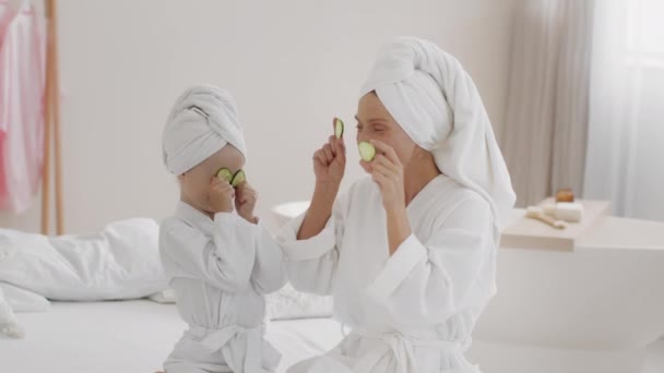 美丽的一天在家里 快乐嬉闹的母亲和女儿穿着浴袍 头戴毛巾 头戴新鲜黄瓜片 在家里放松 慢动作 自由自在 — 图库视频影像