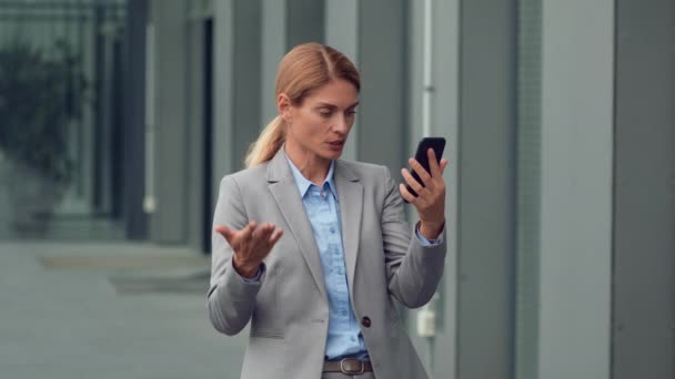 紧急商务谈判 严肃的中年妇女通过智能手机与伴侣聊天 讨论战略计划 站在办公楼附近 慢动作 自由自在 — 图库视频影像