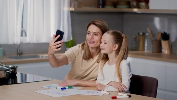 家庭博客内容 漂亮的妈妈在智能手机上和她可爱的小女儿自拍 在厨房里摆出姿势 微笑着一起摆出相机 慢动作 — 图库视频影像