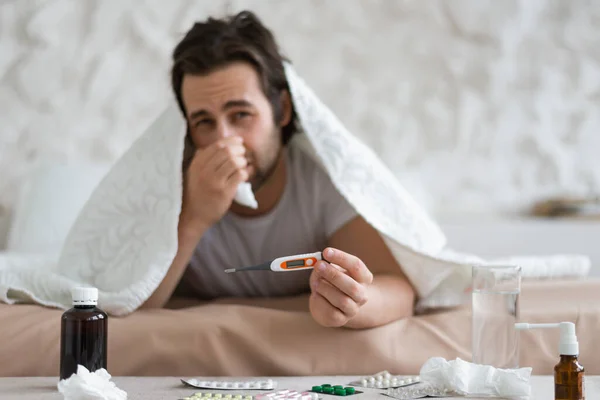 闷闷不乐的欧洲千年人 鼻涕沾满餐巾 躺在床上盖着毯子 用空白屏风显示温度计 在卧室里发烧 家里的流感和感冒 — 图库照片