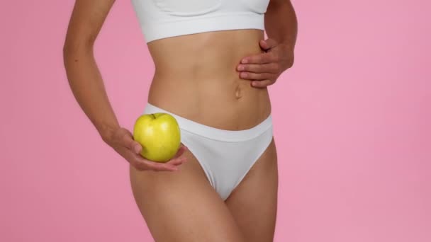 健康营养概念 特写镜头 穿着内衣裤 展示有机苹果 展示其运动身材 粉色背景 动作缓慢 自由自在的瘦弱女子 — 图库视频影像