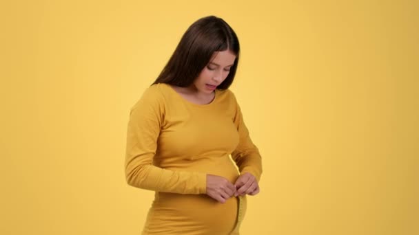 快速的怀孕成长 年轻的孕妇测量她的大肚子 由于体重增加 橙色工作室的背景 慢动作 空虚的空间而感到震惊和不安 — 图库视频影像