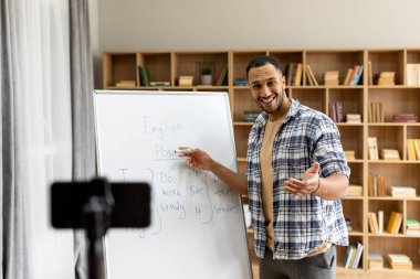 Sanal sınıf, ders ve eğitim, evde eğitim. Beyaz tahtayı gösteren mutlu Arap erkek öğretmen oturma odasındaki web kamerasına bakıyor ve konuşuyor.