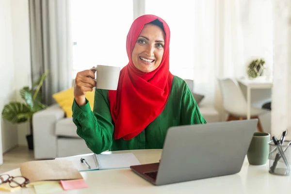 Glückliche Islamische Reife Frau Die Laptop Benutzt Und Morgenkaffee Trinkt — Stockfoto