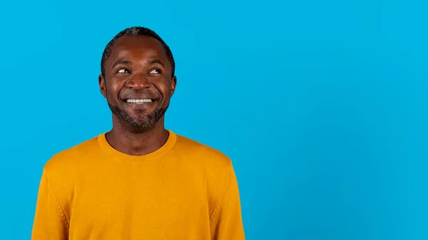 由好奇而快乐的非洲裔美国成熟男人拍摄的头像 他看着复制的空间 在蓝色的工作室背景 全景和网页横幅上观看着惊人的广告 — 图库照片