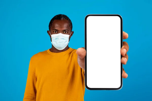戴防护口罩的成熟黑人男子的脸显示智能手机与空白白屏 显示应用程序与考拉病毒爆发跟踪地图 蓝色工作室背景 — 图库照片