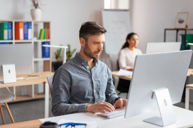 Modern ofis içi, fotokopi alanındaki işyerindeki bilgisayarda daktilo yazan yakışıklı Avrupalı adam yöneticisi. İş, finans planlaması, veri analizi, şirket ve proje çalışmalarında geliştirme