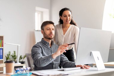 Neşeli genç beyaz erkek menajer modern ofis içinde elleri bilgisayar başında olan bayana boş yer gösteriyor. İş takım çalışması, finans planı, veri analizi, şirkette gelişme ve birlikte çalışma