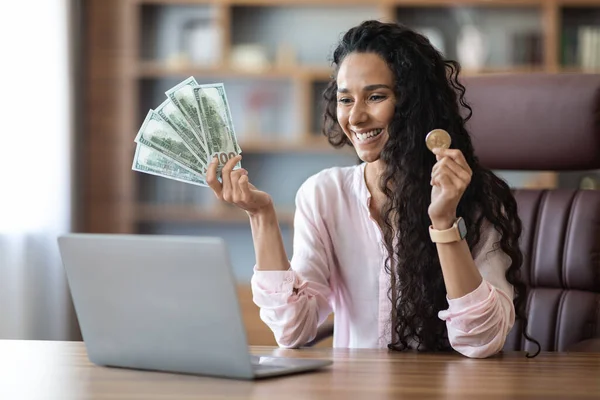 快乐迷人的年轻女人坐在总公司的笔记本电脑前 在股票和市场上赌博 展示比特币和大量的现金 加密交易成功的概念 — 图库照片
